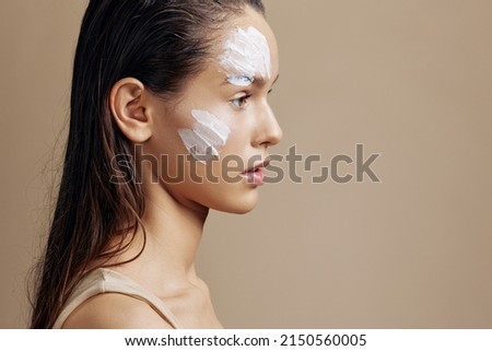 beautiful woman applying a soothing face mask cosmetic beige background