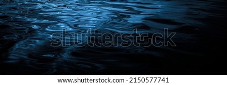      Navy blue water surface. Reflection of light. Ripples and waves. Night. Beautiful dark water background with copy space for design. Web banner. Panoramic. Close-up.                                Royalty-Free Stock Photo #2150577741