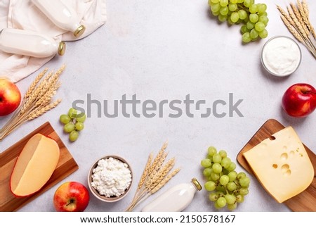 Shavuot flat lay frame with dairy products, first fruits and wheat on light gray background. Jewish Shavuot holiday frame with dairy foods and fruits, top view Royalty-Free Stock Photo #2150578167