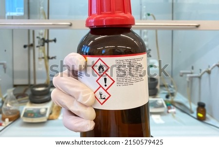A laboratory technician holding a bottle of dangerous chemical agent that poses an environmental risk and is easily flammable.
