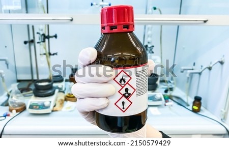 A laboratory technician holding a bottle of dangerous chemical agent that poses an environmental risk and is easily flammable. Royalty-Free Stock Photo #2150579429