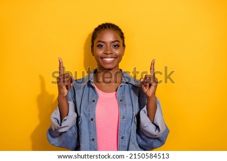 Photo of young cheerful girl indicate fingers empty space recommend select banner isolated over yellow color background