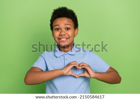 Portrait of handsome cheerful pre-teen boy showing heart symbol amour date feelings isolated over green color background