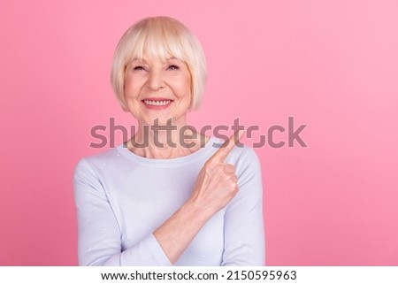 Photo of mature cheerful woman indicate finger empty space promo choice way isolated over pink color background