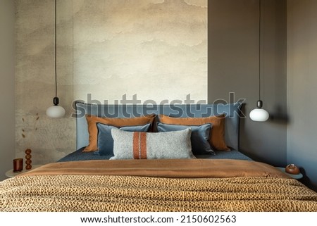 Stylish composition of modern bedroom interior. Bed, creative lamp and elegant personal accessories. Concrete wall. Brown sheeets. Minimalistic masculine concept. Template. Royalty-Free Stock Photo #2150602563