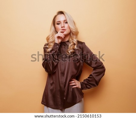Lifestyle, fashion and people concept: Beautiful young blond woman pose for a photo in trendy clothes over beige background.