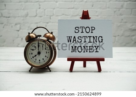 Stop Wasting Money text and alarm clock on white brick wall and wooden background