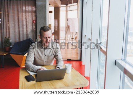 Smart young man looking for information on a website and working as a freelancer on developing a graphic project on a modern laptop using a wireless internet connection in a cafe interior