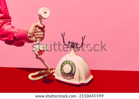 On the line. Pop art photography. Retro objects, gadgets. Female hand holding handset of vintage phone isolated on pink and red background. Vintage, retro 80s, 70s style. Complementary colors.