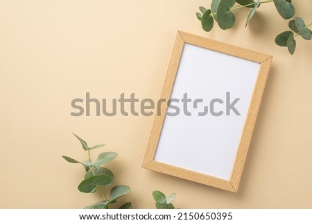 Top view photo of wooden photo frame and eucalyptus on isolated beige background with blank space