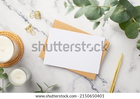 Business concept. Top view photo of candles on rattan serving mat paper sheet craft paper envelope gold pen binder clips and ceramic vase with eucalyptus on white marble background with copyspace