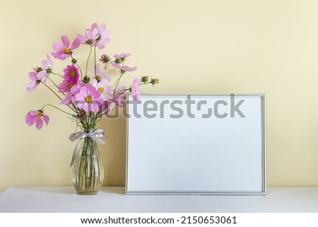 Large silver horizontal A4 mockup blank frame with pink summer flowers in glass vase on yellow wall background.