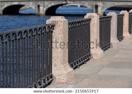 Fence on the embankment of the Fontanka River, granite pillars with a forged fence against the background of the spans of the bridge, in the city of St. Petersburg, Russia
