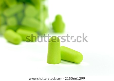 Light green earplugs in the foreground and a jar of earplugs in the background on a white background. Soft foam ear plugs.Close-up.Hearing protection conceptCopy space.High quality photo