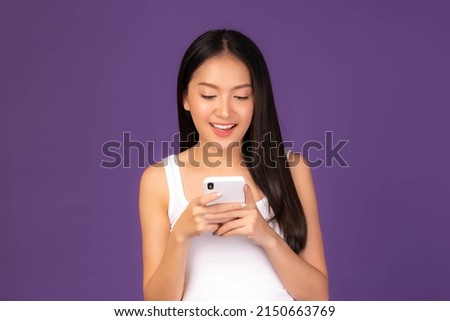Beautiful Asian brunette woman cute girl in white tank top playing a smart phone isolated on purple background - mobile phone uses a online banking for pay online shopping