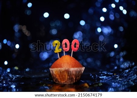 Digital gift card birthday concept. Tasty homemade vanilla anniversary cupcake with number 200 two hundred on aluminium foil and blurred bright background in minimalistic style. High quality image