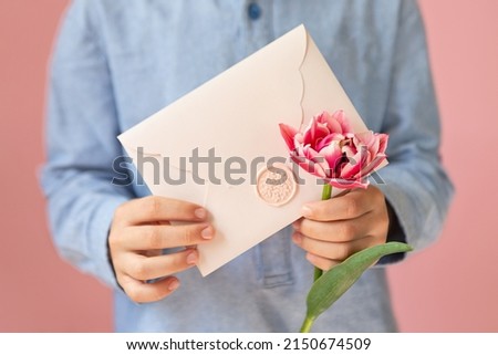 Anonymous child holding pink envelope with gift certificate and tulip in his hands.Mother day concept or present for moms.