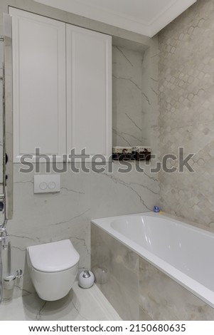 Corner of a bright modern toilet in white tiles with toilet and bath