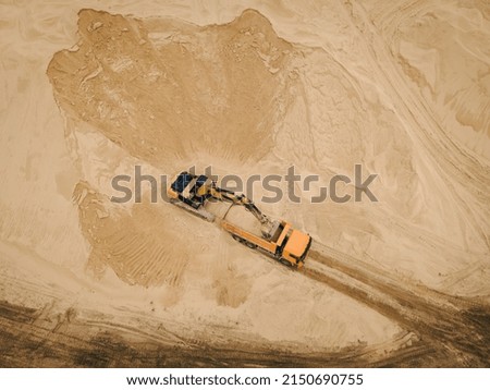 Aerial top down view of an excavator loading sand into a dump truck in opencast sand quarry