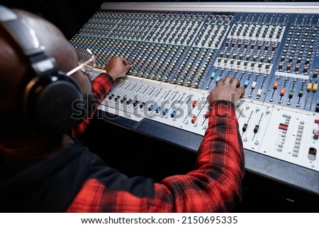 Professional sound engineer producing recording in studio adjusting sound settings at mixing console Royalty-Free Stock Photo #2150695335