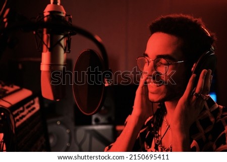 Portrait of young African American singer working in recording studio standing in front of microphone with pop filter enjoying singing