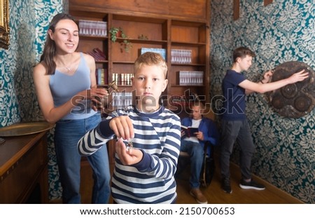Cute interested preteen boy holding key in closed quest room stylized as ancient home library on background with his family