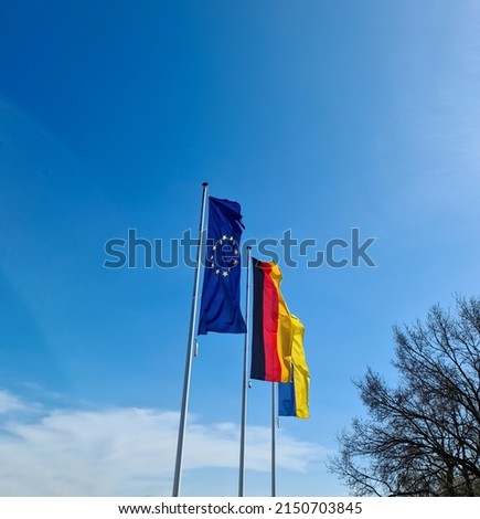 Flags of Ukraine, Germany and European Union fly side by side against blue sky