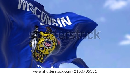The US state flag of Wisconsin waving in the wind. Wisconsin is a state in the upper Midwestern United States. Democracy and independence. Royalty-Free Stock Photo #2150705331