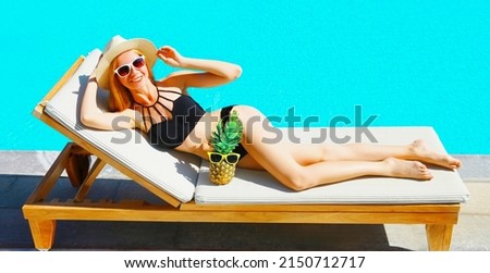 Summer vacation, happy young woman lying on deckchair with pineapple on pool background