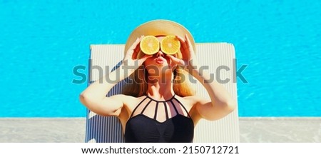 Summer portrait of woman covering her eyes with fresh slices of orange lying on deck chair on pool background
