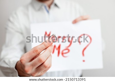 man holding a piece of paper with the inscription will you marry me and a ring on a white background