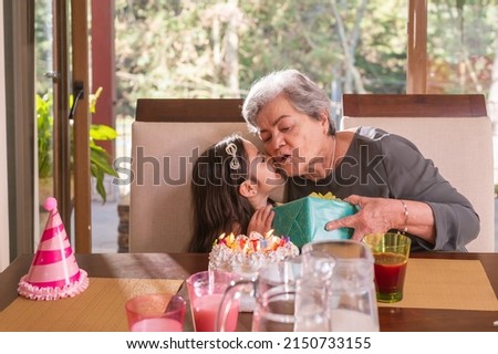 Hispanic grandmother and granddaughter. Granddaughter kisses her grandmother and gives her a birthday present.