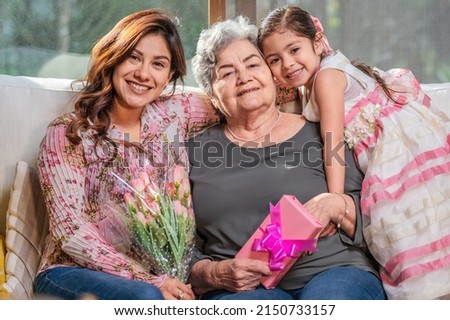 Happy Mother's Day! Latin girl mom and grandmother giving flowers and gifts. Grandma, mom, and little girl smiling and hugging.