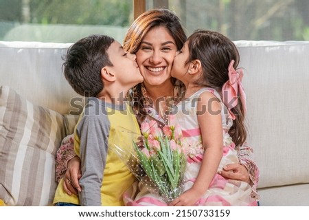 Mother's Day.  Latin mother holds her two children, a boy, and a girl, as they hug and kiss her. Royalty-Free Stock Photo #2150733159