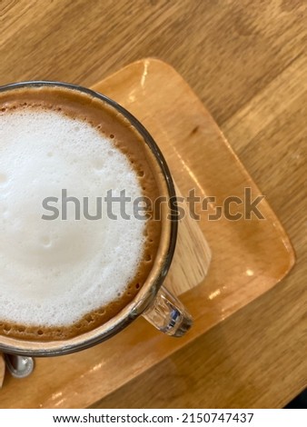 Top view of a cup of cappuccino with cream foam on top and the coffee in the wooden tray on the table