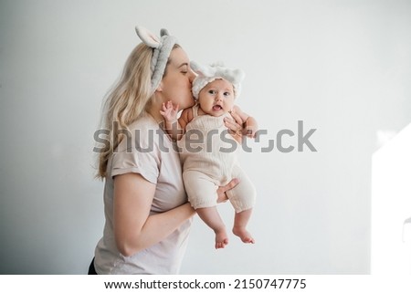 mom blonde and newborn daughter in white with rabbit ears photo on a light background celebrate Easter. High quality photo