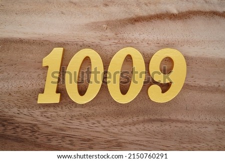 Wooden  numerals 1009 painted in gold on a dark brown and white patterned plank background.
