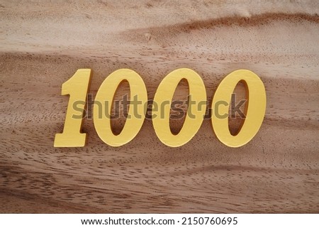 Wooden  numerals 1000 painted in gold on a dark brown and white patterned plank background.