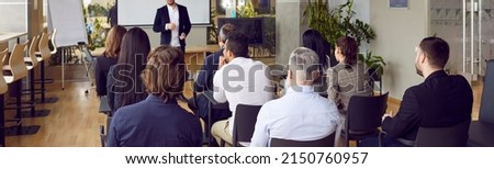 Audience at conference hall. Rear view of people on business training listening to male coach who lectures and trains staff. Business and entrepreneurship concept. Banner. Panorama.