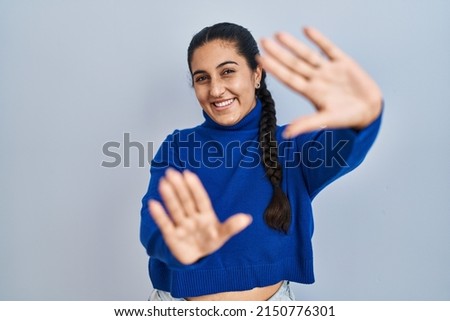 Young hispanic woman standing over isolated background doing frame using hands palms and fingers, camera perspective 