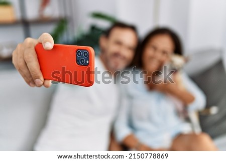 Middle age man and woman couple make selfie by the smartphone sitting on sofa with dog at home