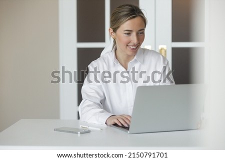 Portrait of a positive girl sitting at a table with a laptop in the office. A business woman works with a laptop and smiling to the camera.