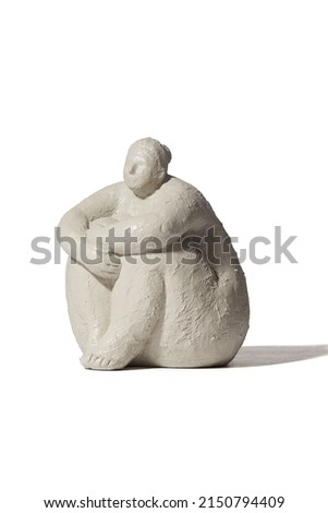 Detail shot of a figurine of a paleolithic venus sitting with her hands on her knees. The white statuette is isolated on the white background.