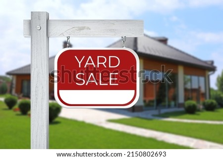 Sign with text YARD SALE and blurred view of modern house on sunny day