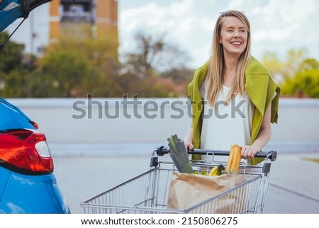 Beautiful young woman shopping in a grocery store supermarket, putting the groceries into her car in the parking lot. Woman after shopping and driving home now with her car outdoor.