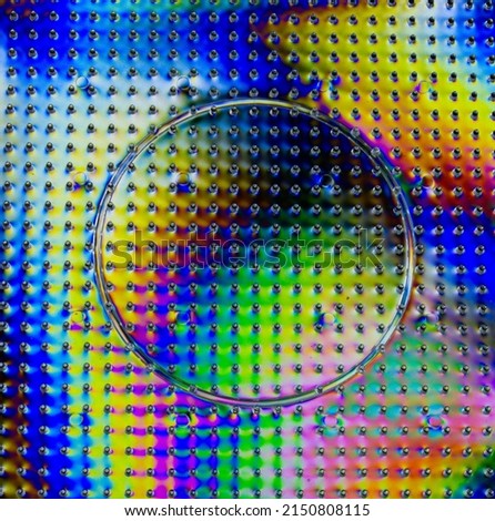 A photograph of transparent plastic with special effects caused by the double polarization of light. An abstract image of a circle within a square with raised dots, multicolored. NOT an illustration.