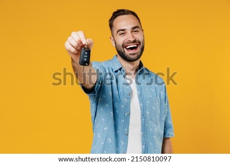 Young smiling happy caucasian man 20s wearing blue shirt white t-shirt hold give car key fob keyless system look camera isolated on plain yellow background studio portrait. People lifestyle concept Royalty-Free Stock Photo #2150810097