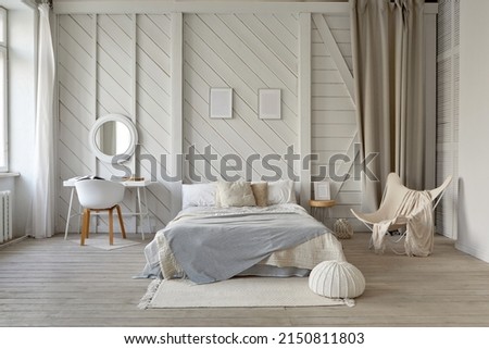 Comfortable bed with blanket and cushions placed on rug at wall with decorative frames in stylish bedroom with table and armchair in pastel colors Royalty-Free Stock Photo #2150811803