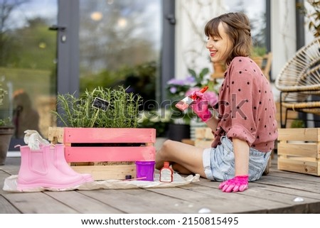 Young woman painting wooden box in pink color, doing some renovating housework on the terrace outdoors. DIY concept Royalty-Free Stock Photo #2150815495