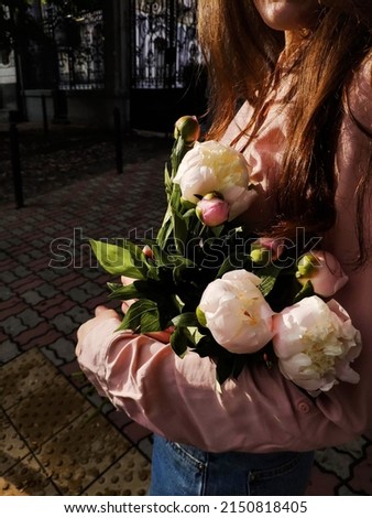Brunette woman with peonies flowers in her hands in springtime outside near beautiful gates